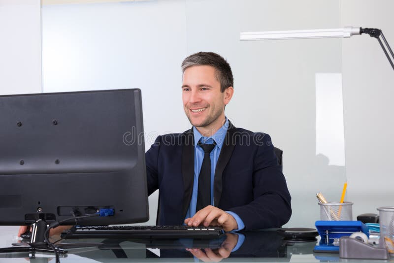 Homem de negócios feliz que usa o computador em seu escritório foto de stock royalty free Homem de negócios feliz que usa o computador em seu escritório foto de stock royalty free