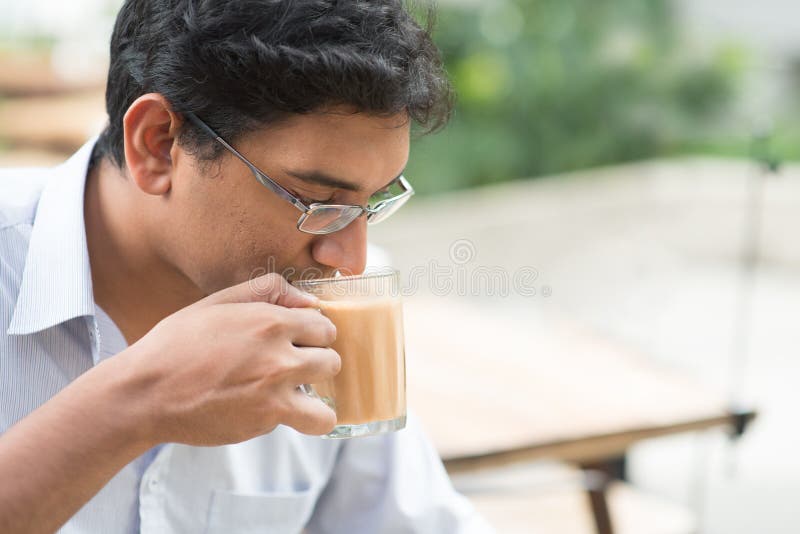 Homem de negócios indiano que sorve um chá quente do leite do copo imagem de stock Homem de negócios indiano que sorve um chá quente do leite do copo imagem de stock