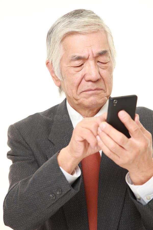 Homem de negócios japonês superior que usa o telefone esperto que olha confundido foto de stock Homem de negócios japonês superior que usa o telefone esperto que olha confundido foto de stock