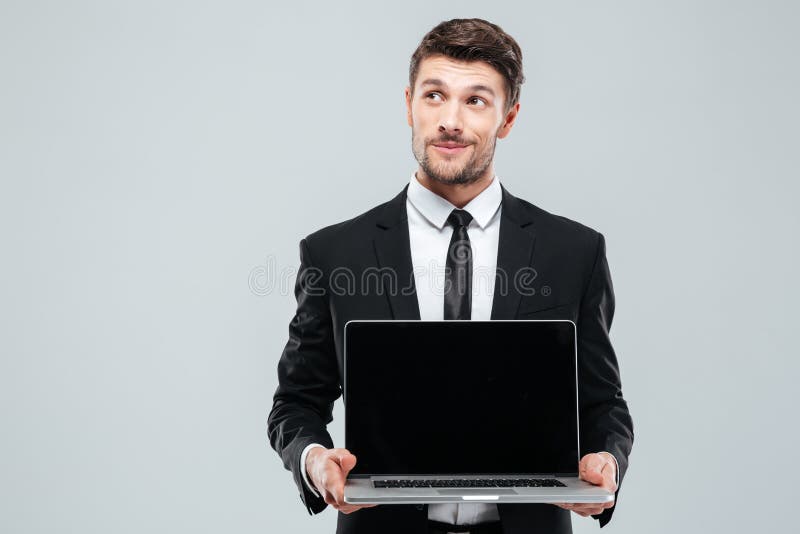 Homem de negócios novo pensativo que guarda o portátil e o pensamento da tela vazia imagens de stock Homem de negócios novo pensativo que guarda o portátil e o pensamento da tela vazia imagens de stock