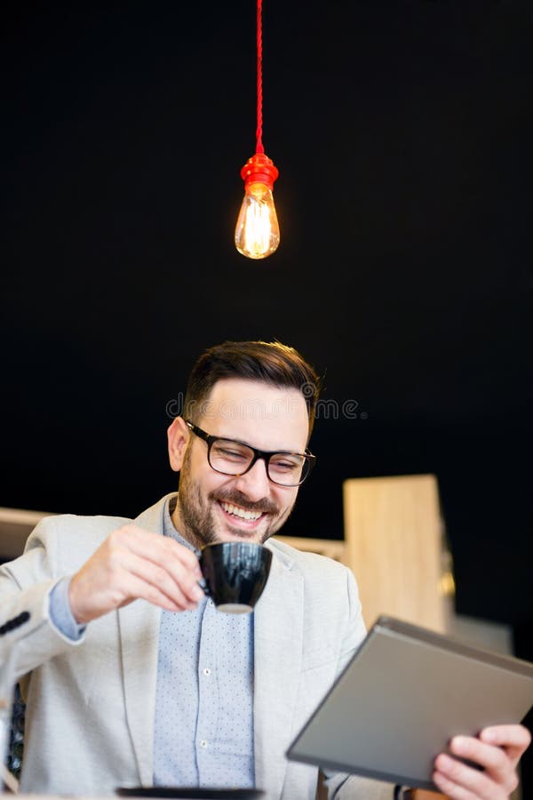 Homem de negócios novo que usa uma tabuleta e bebendo o café ao trabalhar em uma cafetaria moderna foto de stock royalty free Homem de negócios novo que usa uma tabuleta e bebendo o café ao trabalhar em uma cafetaria moderna foto de stock royalty free