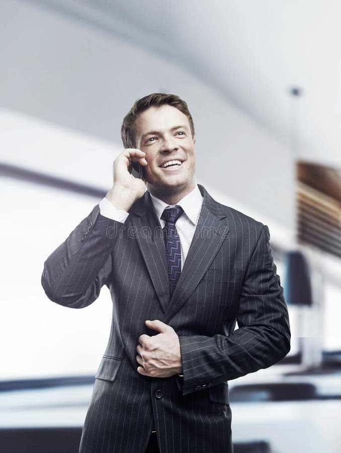 Homem de negócios que fala na posição móvel no escritório imagem de stock royalty free Homem de negócios que fala na posição móvel no escritório imagem de stock royalty free