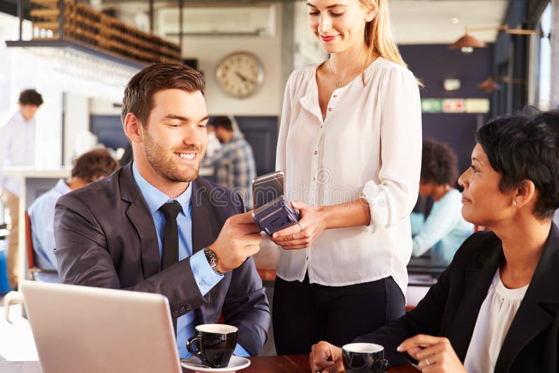Homem de negócios que faz o pagamento pelo telefone em um café imagem de stock royalty free Homem de negócios que faz o pagamento pelo telefone em um café imagem de stock royalty free