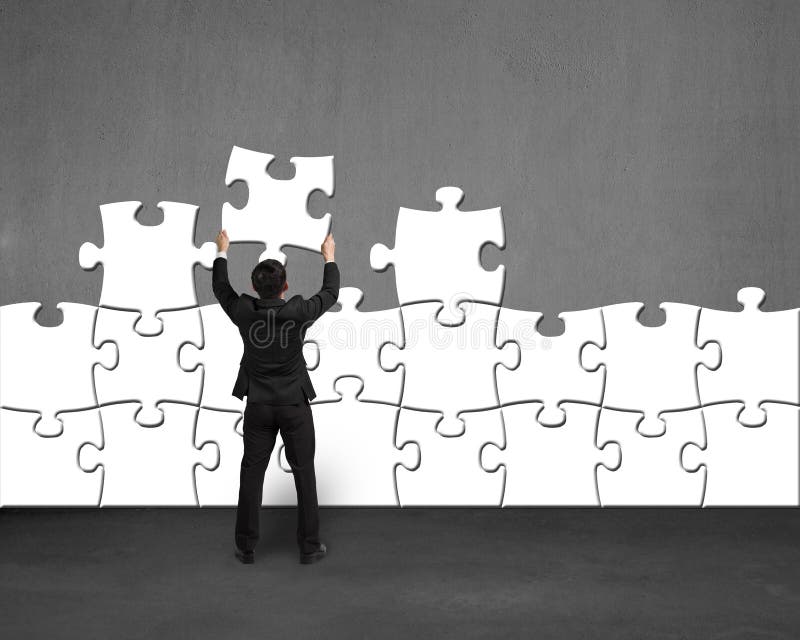 Businessman holding white puzzle to assemble on concrete wall. Businessman holding white puzzle to assemble on concrete wall