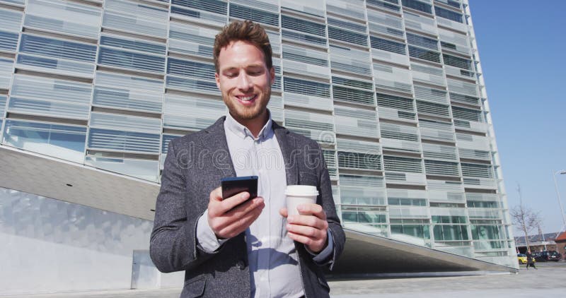 Homem de negócios sorridente usando telefone e tomando café enquanto caminhava na construção