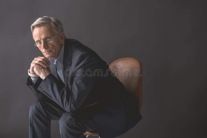 Homem de negócios velho pensativo que localiza na cadeira fotos de stock royalty free Homem de negócios velho pensativo que localiza na cadeira fotos de stock royalty free