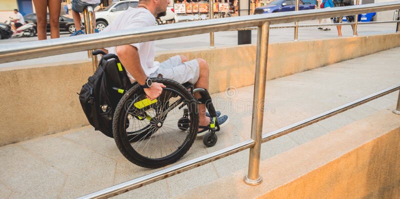 Homem deficiente numa cadeira de rodas move-se numa rampa para a praia.