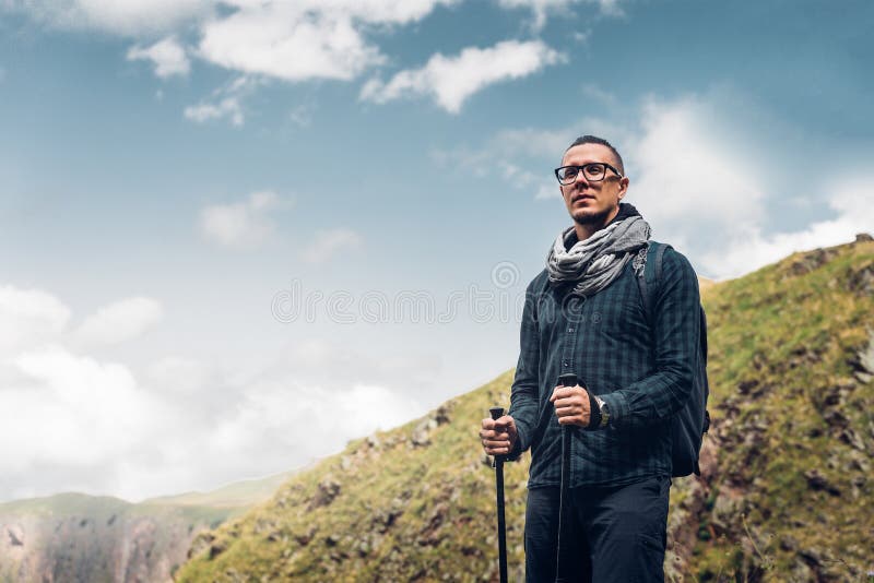 Homem do caminhante com trouxa e Polos Trekking que descansam e que olham A foto de stock Homem do caminhante com trouxa e Polos Trekking que descansam e que olham A foto de stock