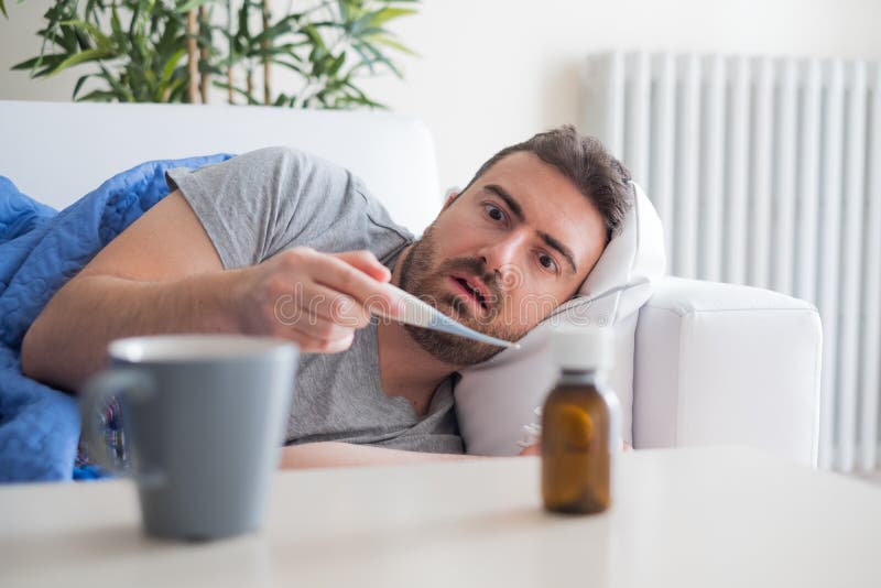 Homem doente que verifica a temperatura e que sente mau em casa fotos de stock Homem doente que verifica a temperatura e que sente mau em casa fotos de stock