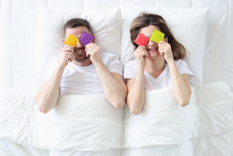 Homem e mulher estão segurando preservativos coloridos enquanto deitados na cama