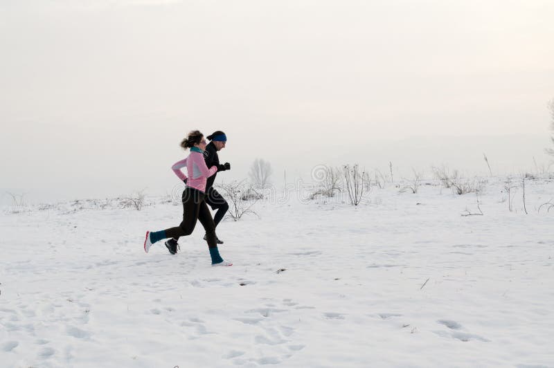 Homem e mulher que correm na neve fotografia de stock Homem e mulher que correm na neve fotografia de stock