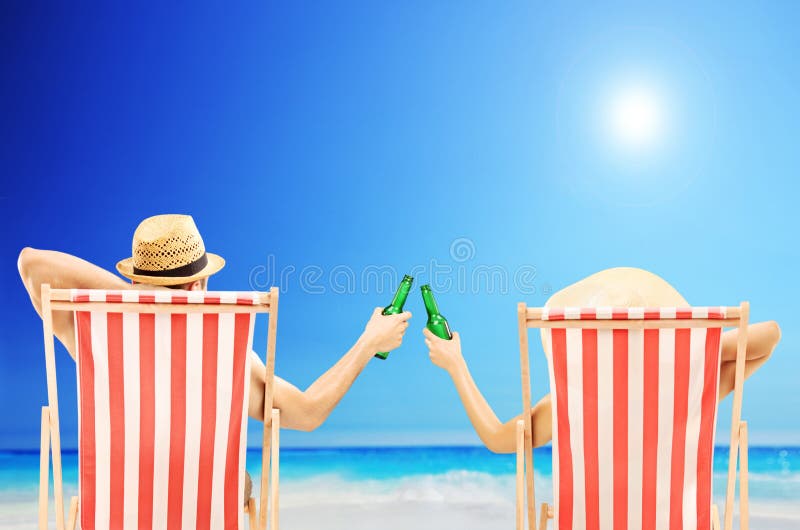 Homem e mulher que relaxam em uma praia e que cheering com cervejas imagem de stock Homem e mulher que relaxam em uma praia e que cheering com cervejas imagem de stock
