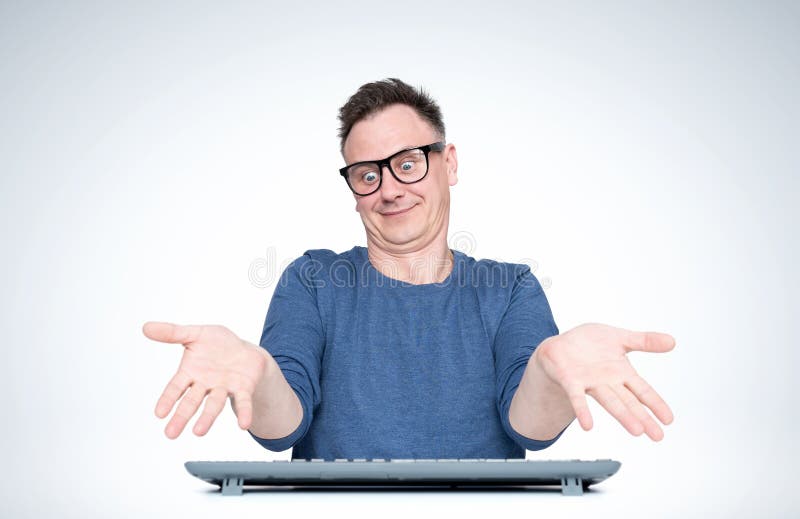 Homem em trabalhos dos vidros no computador, espalha suas mãos em um gesto que eu não sei, no fundo claro Front View fotografia de stock Homem em trabalhos dos vidros no computador, espalha suas mãos em um gesto que eu não sei, no fundo claro Front View fotografia de stock