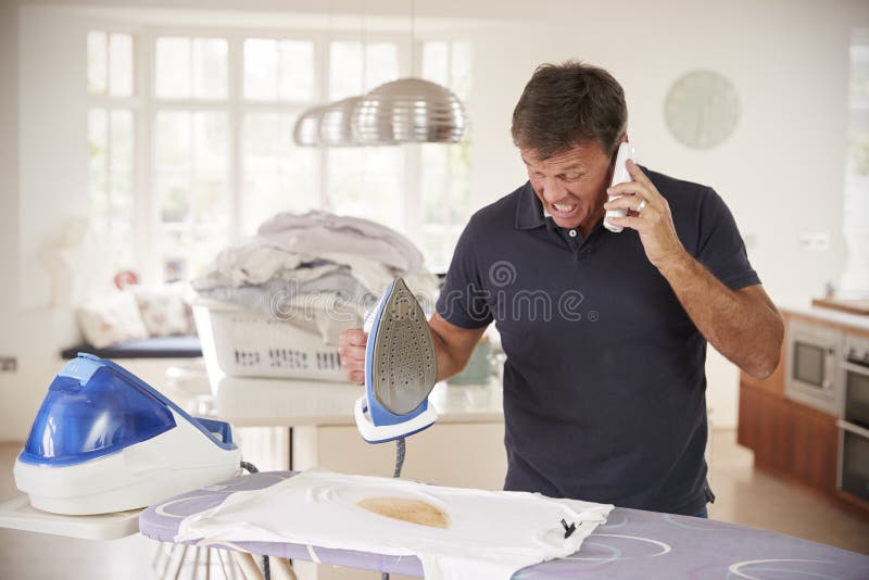 Homem envelhecido meio confundido pelo telefone quando passar queimar a camisa imagem de stock Homem envelhecido meio confundido pelo telefone quando passar queimar a camisa imagem de stock