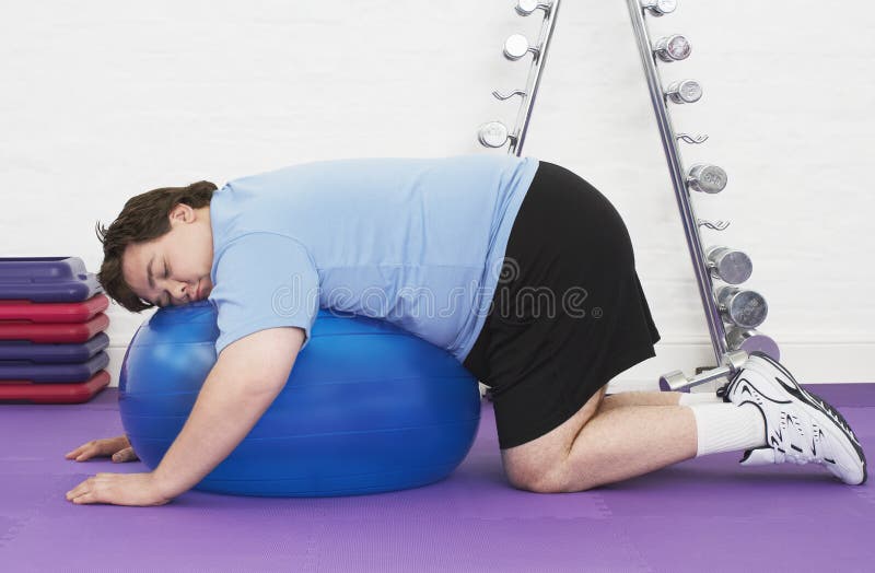 Homem excesso de peso que dorme na bola do exercício imagens de stock Homem excesso de peso que dorme na bola do exercício imagens de stock