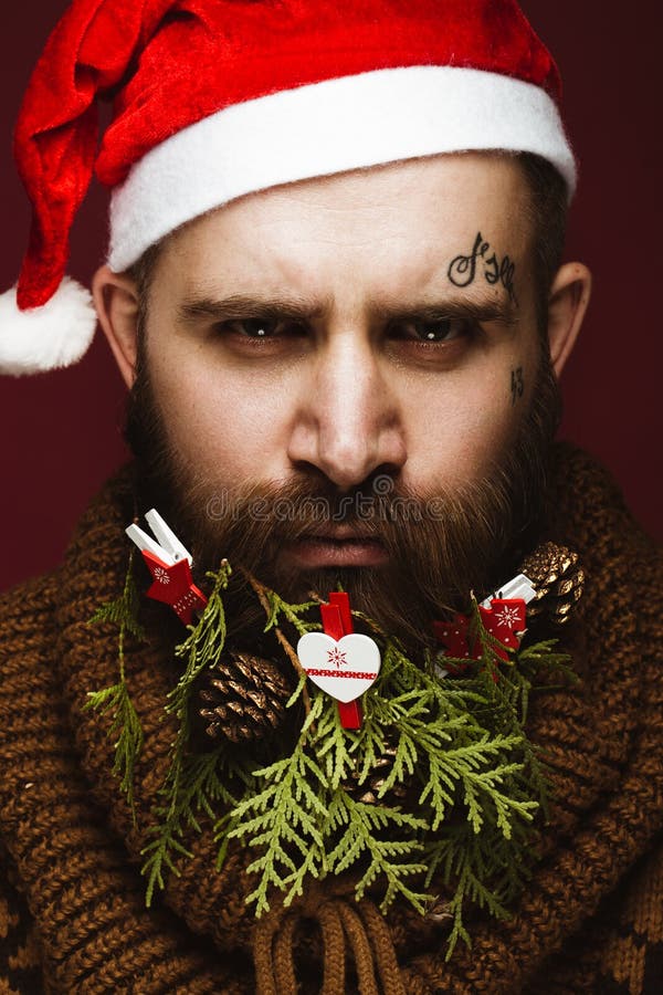 Homem farpado engraçado em uma imagem do ` s do ano novo como Santa Claus com as decorações em sua barba Festa do Natal imagem de stock royalty free Homem farpado engraçado em uma imagem do ` s do ano novo como Santa Claus com as decorações em sua barba Festa do Natal imagem de stock royalty free