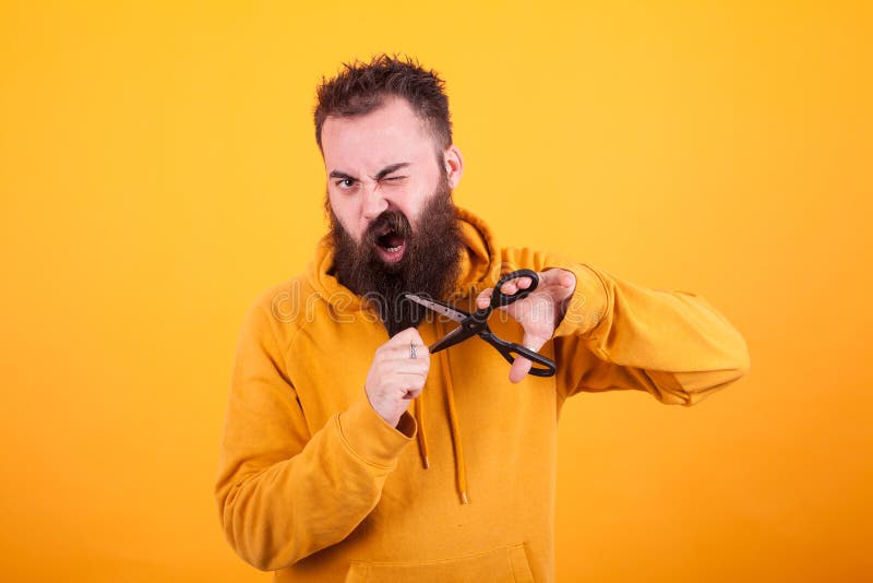 Homem farpado fresco que olha terrificado ao cortar sua barba sobre o fundo amarelo fotografia de stock Homem farpado fresco que olha terrificado ao cortar sua barba sobre o fundo amarelo fotografia de stock