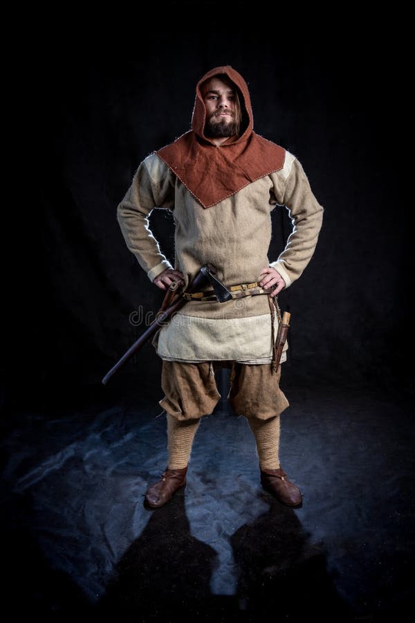 Homem farpado novo em uma roupa e em uma capa da idade de viquingue com um machado fotos de stock Homem farpado novo em uma roupa e em uma capa da idade de viquingue com um machado fotos de stock