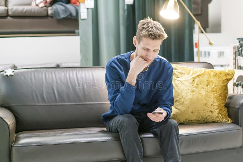 Homem farpado novo que usa o smartphone que senta-se no sofá f foto de stock Homem farpado novo que usa o smartphone que senta-se no sofá f foto de stock