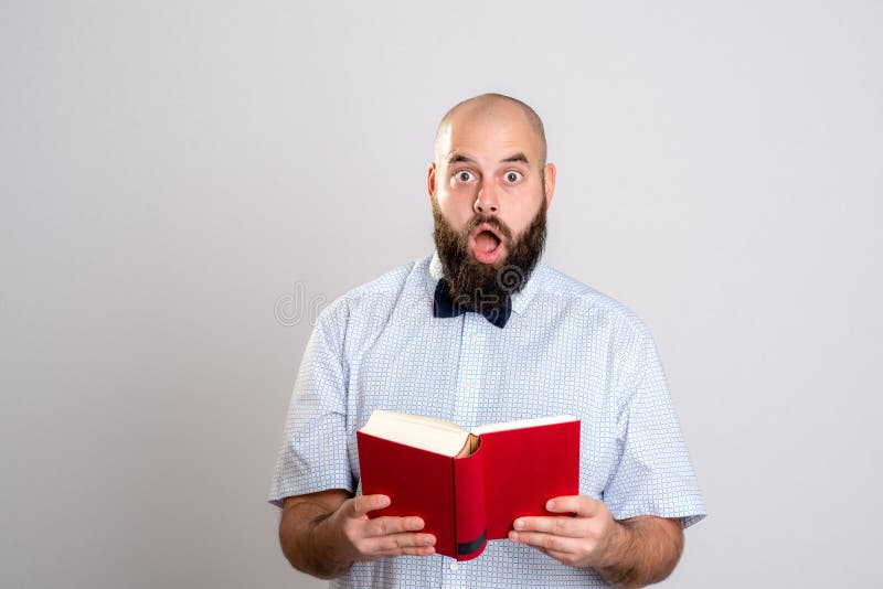 Homem farpado que lê um livro na frente do fundo cinzento imagem de stock Homem farpado que lê um livro na frente do fundo cinzento imagem de stock