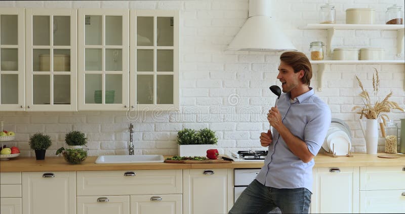 Homem feliz bonito cantando e dançando sozinho na cozinha moderna