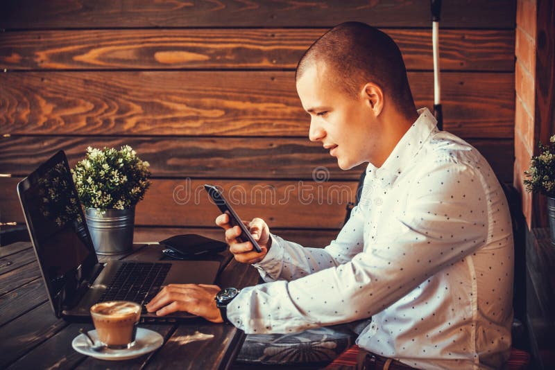 Homem feliz independente que trabalha com um portátil e um telefone esperto foto de stock Homem feliz independente que trabalha com um portátil e um telefone esperto foto de stock