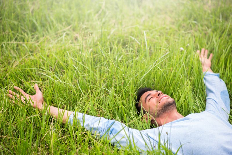 Homem feliz que encontra-se na grama verde com os braços estendidos