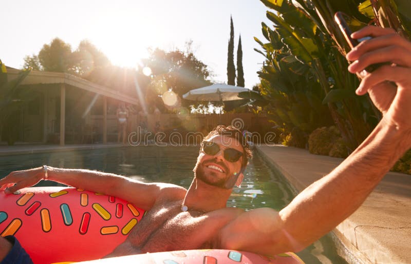 Homem flutuando em anel inflável na festa da piscina de verão tomando selfie no telefone celular