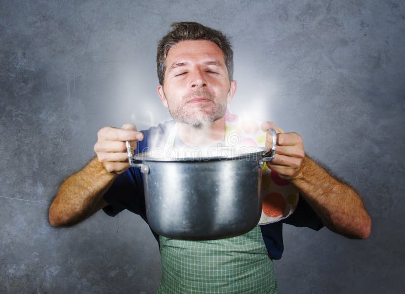 Homem home feliz e orgulhoso atrativo novo do cozinheiro que cozinha a sopa que guarda o potenciômetro da cozinha que cheira gest fotografia de stock Homem home feliz e orgulhoso atrativo novo do cozinheiro que cozinha a sopa que guarda o potenciômetro da cozinha que cheira gest fotografia de stock