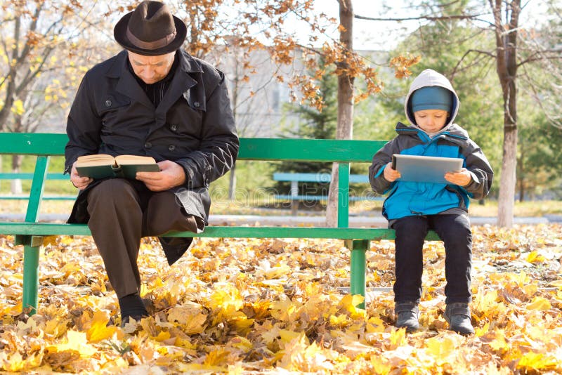 Homem idoso e menino pequeno que compartilham de um banco de parque fotos de stock Homem idoso e menino pequeno que compartilham de um banco de parque fotos de stock