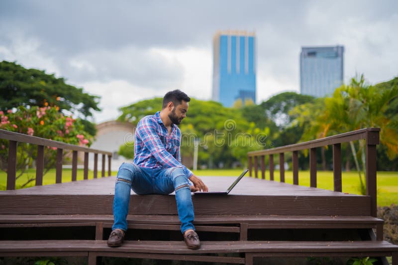 Homem indiano considerável novo no parque usando o laptop fotos de stock Homem indiano considerável novo no parque usando o laptop fotos de stock