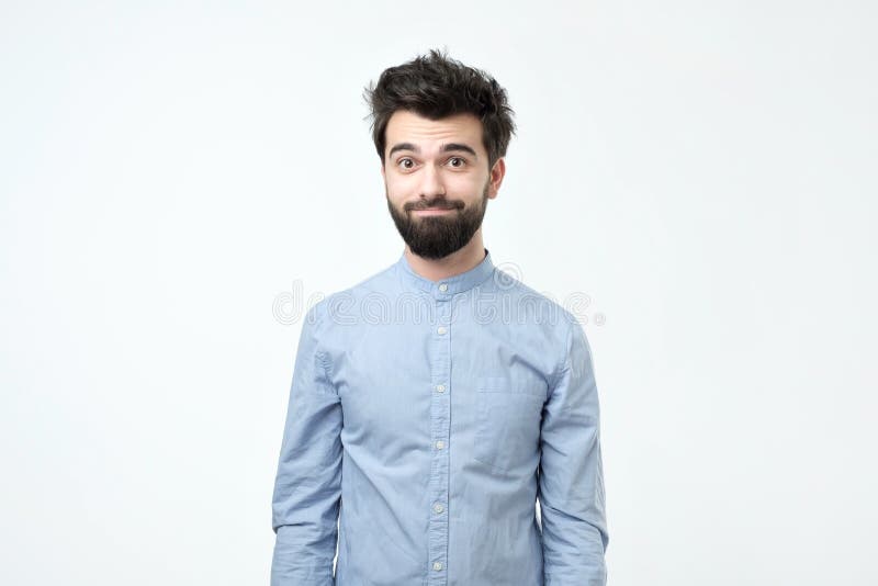 Homem latino-americano cansado na camisa azul com a barba que olha confusamente na câmera imagem de stock Homem latino-americano cansado na camisa azul com a barba que olha confusamente na câmera imagem de stock