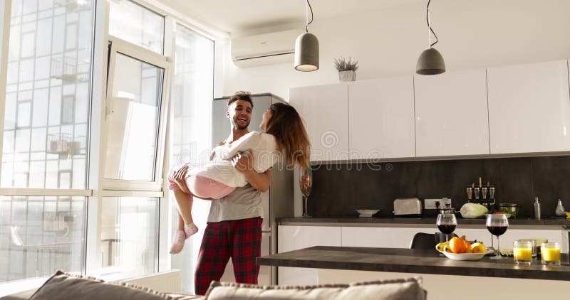 Homem latino-americano de sorriso feliz Carry Asian Woman, par romântico novo que gira Aroud junto na cozinha