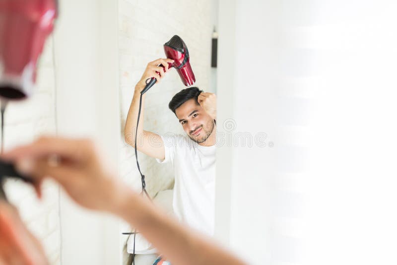 Homem latino que usa Hairdryer em casa fotos de stock Homem latino que usa Hairdryer em casa fotos de stock