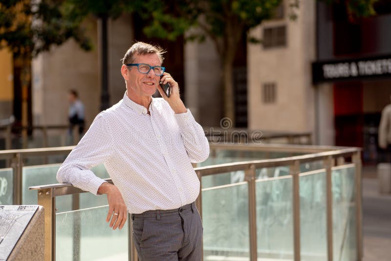 Homem maduro atrativo feliz em seu telefone esperto ao andar no sorriso da rua imagens de stock royalty free Homem maduro atrativo feliz em seu telefone esperto ao andar no sorriso da rua imagens de stock royalty free