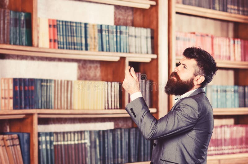 Homem maduro com cara séria O professor está na biblioteca grande e escolhe o livro Homem farpado no terno caro no seu imagens de stock Homem maduro com cara séria O professor está na biblioteca grande e escolhe o livro Homem farpado no terno caro no seu imagens de stock
