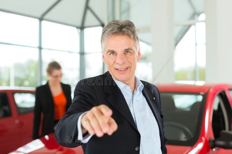 Mature single men with red auto in light car dealership with a female customer, a young woman, he is obviously buying a car or is a car dealer. Mature single men with red auto in light car dealership with a female customer, a young woman, he is obviously buying a car or is a car dealer