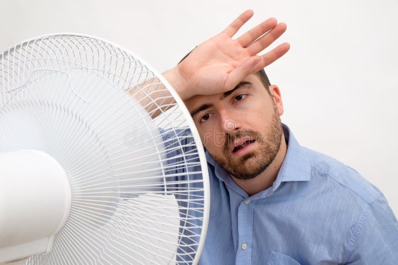 Flushed man feeling hot in front of a big fan. Flushed man feeling hot in front of a big fan