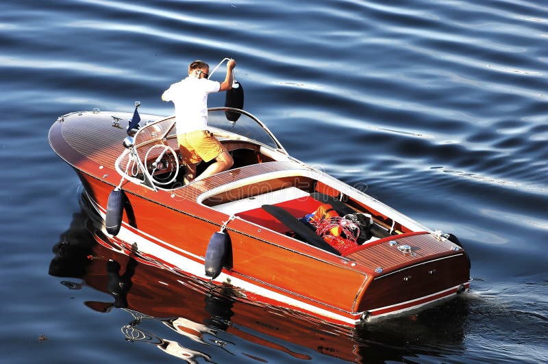 A view of a man setting rubber bumpers on the side of a wooden motorboat in preparation for docking. A view of a man setting rubber bumpers on the side of a wooden motorboat in preparation for docking.