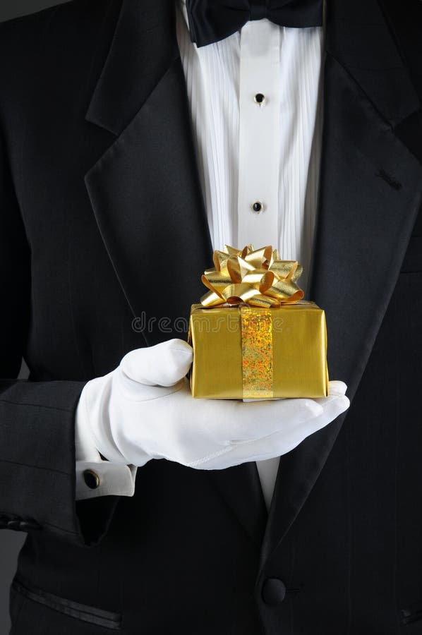 Closeup of a man wearing a tuxedo holding a Chrismas present in front of his body. Vertical format. Man is unrecognizable. Closeup of a man wearing a tuxedo holding a Chrismas present in front of his body. Vertical format. Man is unrecognizable.