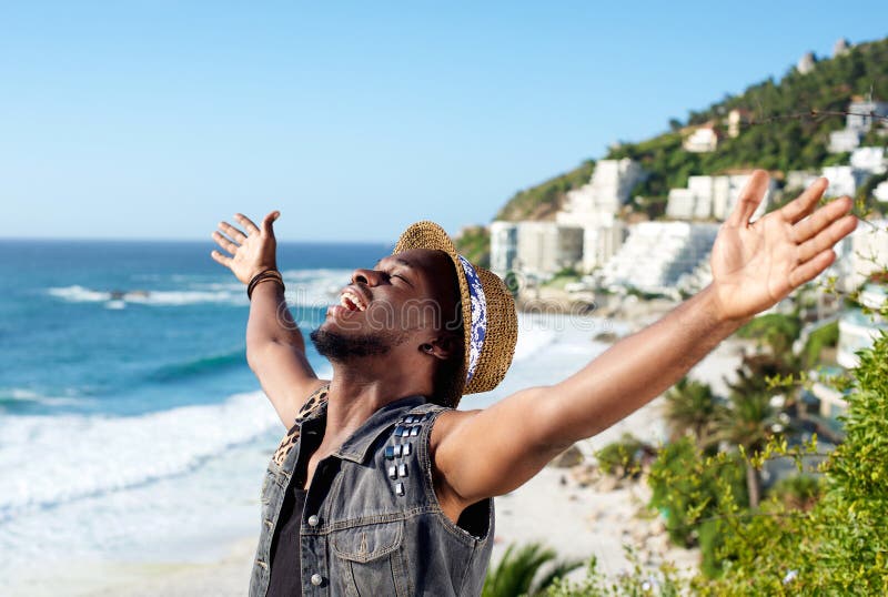 Homem novo alegre com a propagação dos braços aberta na praia imagens de stock Homem novo alegre com a propagação dos braços aberta na praia imagens de stock