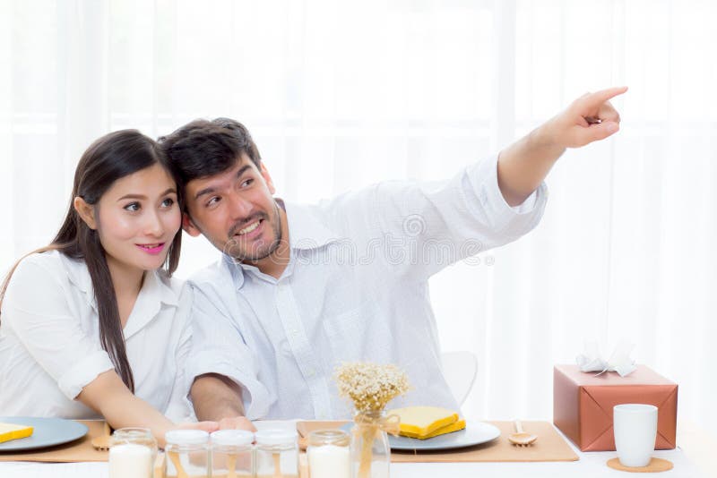 Homem novo alegre e mulher asiáticos que têm o almoço de assento e que falam junto apontando algo foto de stock Homem novo alegre e mulher asiáticos que têm o almoço de assento e que falam junto apontando algo foto de stock