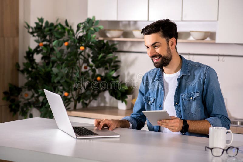 Homem novo alegre que usa seu portátil imagens de stock royalty free Homem novo alegre que usa seu portátil imagens de stock royalty free