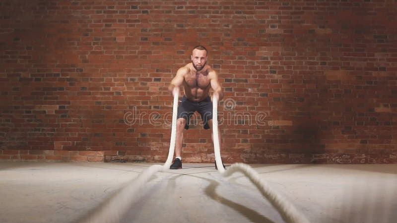 Homem novo atlético com a corda da batalha que faz o exercício no gym de formação funcional da aptidão Movimento lento