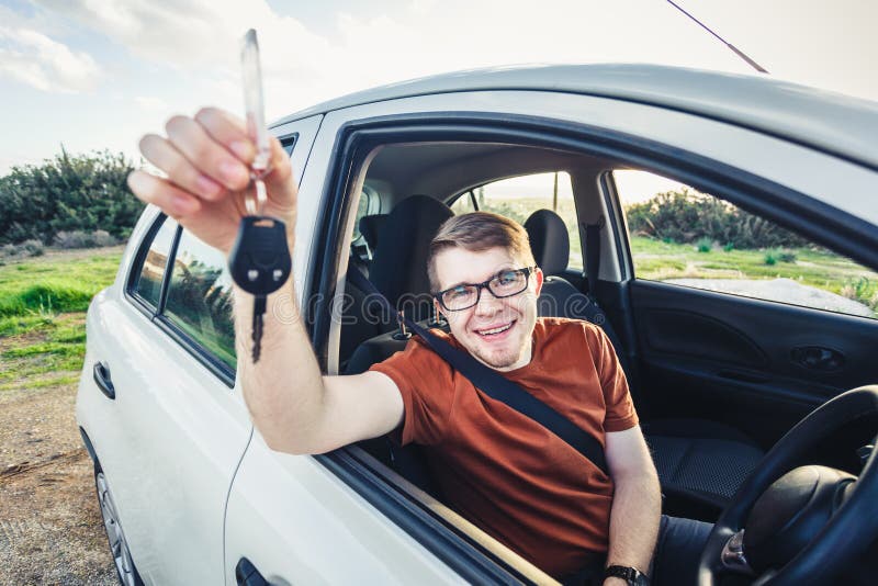 Homem novo atrativo que mostra seus chaves e sorriso novos do carro foto de stock Homem novo atrativo que mostra seus chaves e sorriso novos do carro foto de stock