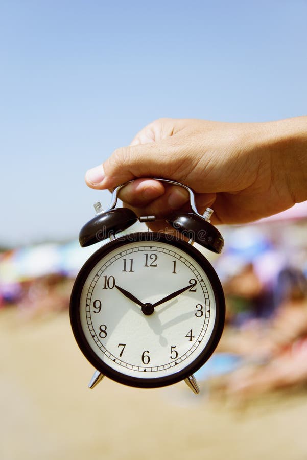 Homem novo com um despertador na praia imagem de stock royalty free