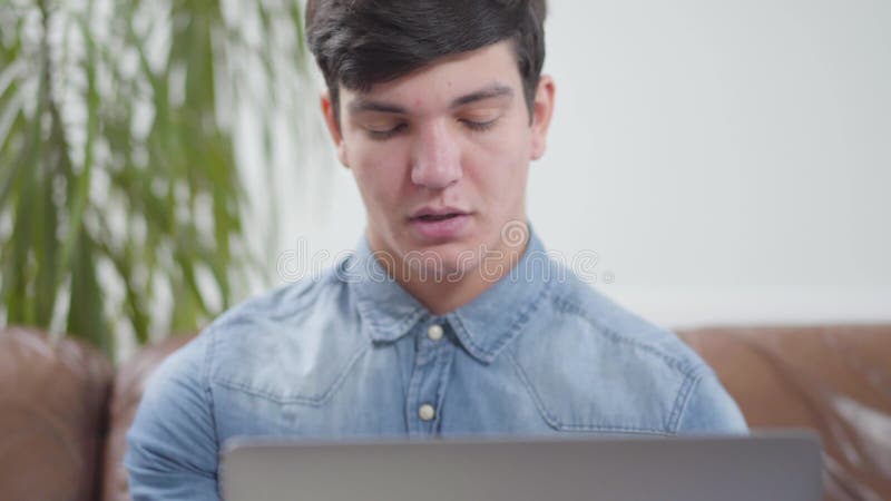 Homem novo considerável do retrato que senta-se na frente do portátil em casa Estudante que verifica a caixa postal Apego aos dis