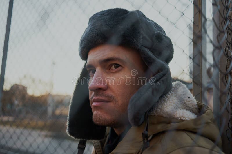 Homem novo considerável feliz no tampão com earflaps O homem novo no chapéu forrado a pele fotografia de stock Homem novo considerável feliz no tampão com earflaps O homem novo no chapéu forrado a pele fotografia de stock