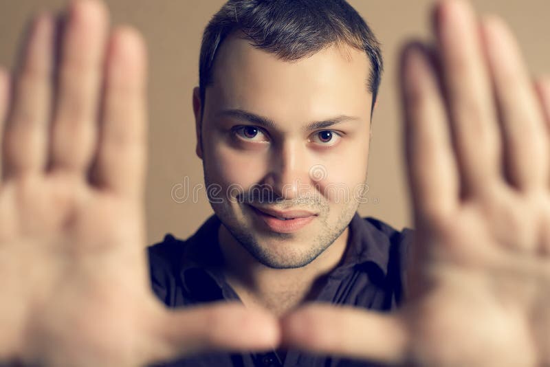 Homem novo considerável que olha a câmera através do quadro imagem de stock royalty free Homem novo considerável que olha a câmera através do quadro imagem de stock royalty free