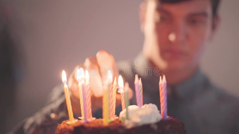Homem novo considerável que senta-se na frente de poucas velas da iluminação do bolo com o isqueiro O indivíduo só tem a festa de